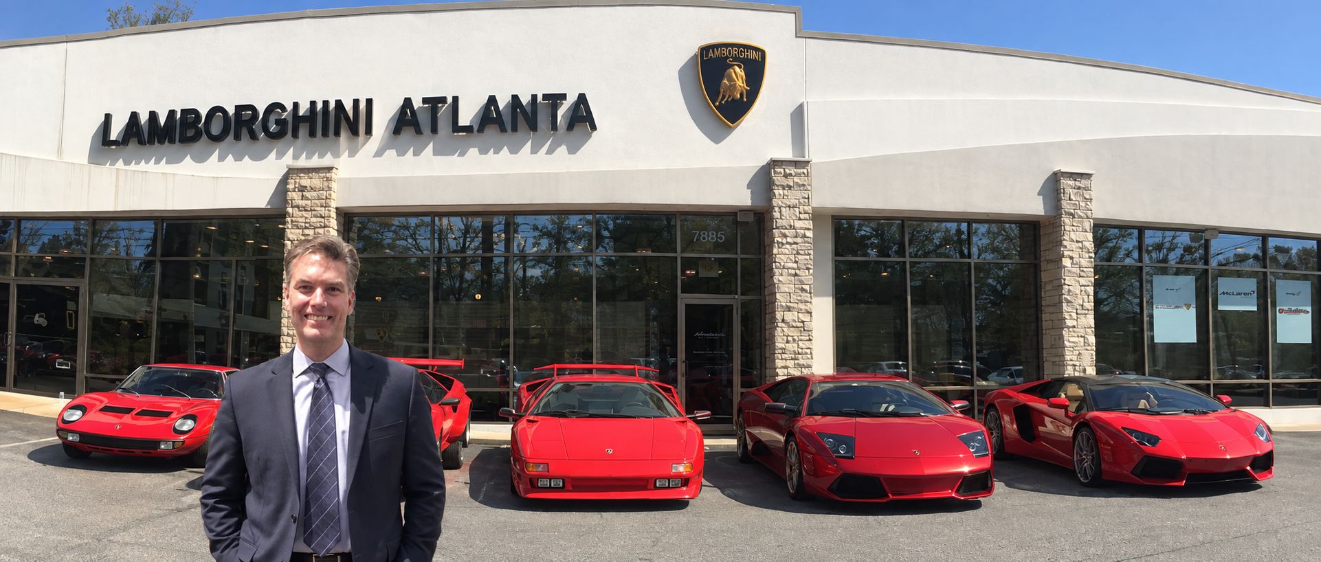 J. Eric Gregory standing in front of a Lamborghini dealership with a row of red Lamborghinis